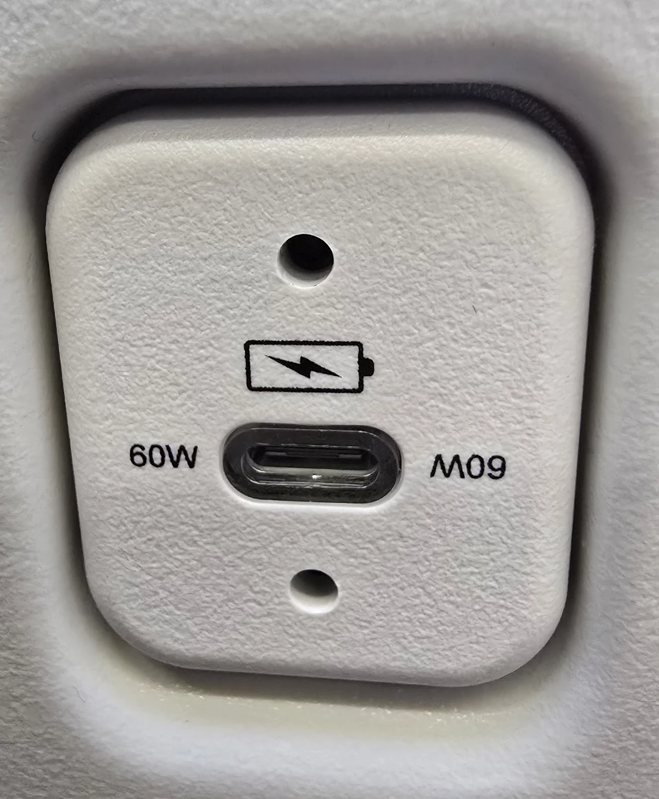 Gniazdo ładowania USB typu C zamontowane w białej powierzchni, oznaczenie ładowania 60W oraz symbol baterii.