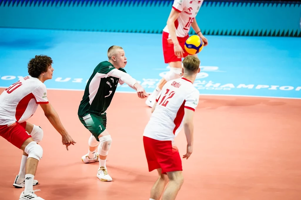 Polska - Włochy U-19 Trzech zawodników w strojach sportowych skupionych na odbiorze piłki podczas meczu siatkówki, jasne boisko z wyraźnie oznaczonymi liniami i charakterystycznymi strojami według drużyn.
