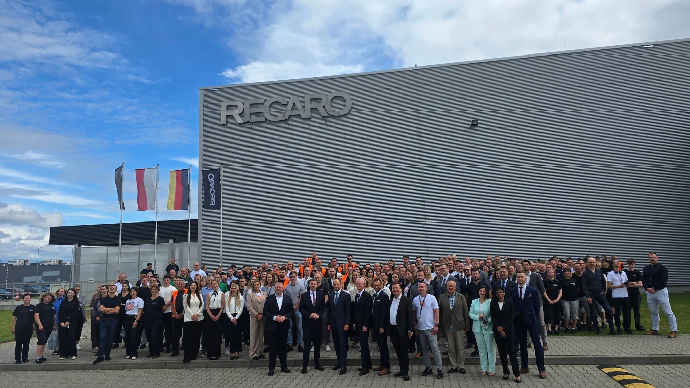 14 tysięcy foteli do samolotów LOT-u wyprodukuje fabryka Recaro ze Świebodzina. Firma zatrudnia 650 pracowników. Duża grupa osób zebrana przed nowoczesnym budynkiem z napisem RECARO, w tle powiewają flagi kilku krajów oraz flaga firmowa, ludzie stoją blisko siebie pozując do pamiątkowego zdjęcia zbiorowego.