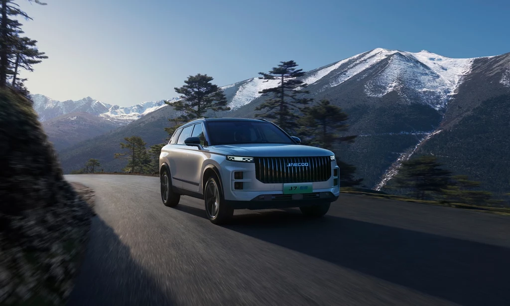 Pracując na wyglądem i sylwetką Jaecoo 7 Super Hybrid, projektanci inspirowali się naturą Srebrny SUV jedzie asfaltową górską drogą otoczoną drzewami, w tle ośnieżone szczyty gór oraz błękitne niebo