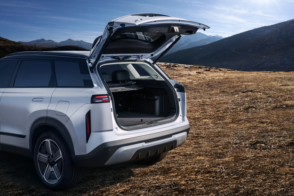 Pojemność bagażnika JAECOO 7 Super Hybrid to 500/1265 litrów SUV z otwartym bagażnikiem ustawiony na suchym, kamienistym terenie z widocznymi wzgórzami i jasnym niebem w tle