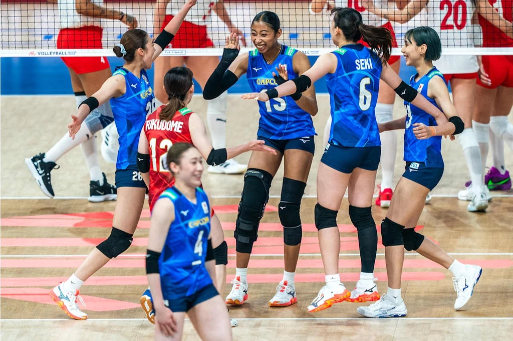 Liga Narodów siatkarek. Drużyna Japonii Grupa zawodniczek w niebieskich strojach siatkarskich świętuje zdobycie punktu na boisku, widoczne uśmiechy oraz gesty radości, w tle drużyna przeciwnicza w zestawie czerwono-białym.