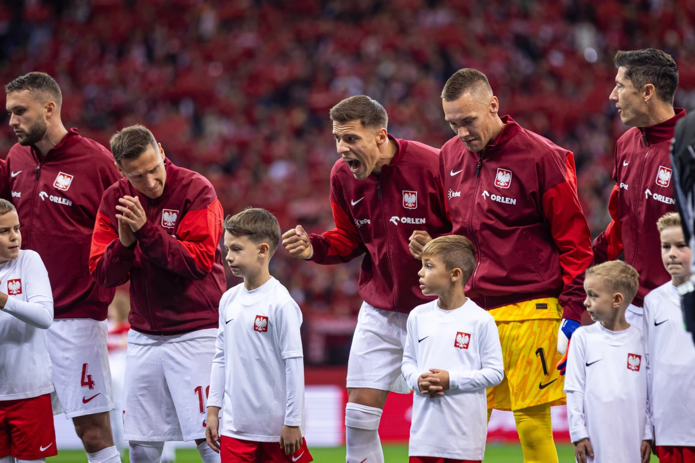 Sebastian Walukiewicz (pierwszy z lewej) ma zamienić Torino na Sassuolo Piłkarze reprezentacji Polski ustawieni na murawie w oficjalnych dresach podczas uroczystości przedmeczowej, obok nich dzieci w białych koszulkach z godłem Polski, w tle wypełniony stadion i kibice.