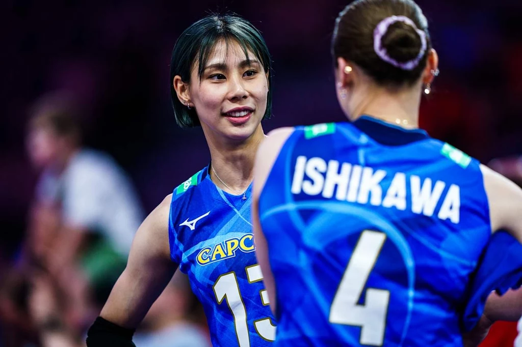 Siatkarki reprezentacji Japonii Dwie zawodniczki drużyny siatkarskiej w niebieskich strojach rozmawiają ze sobą na boisku podczas meczu, na jednym z strojów widoczny jest napis 'ISHIKAWA' oraz numer 4.