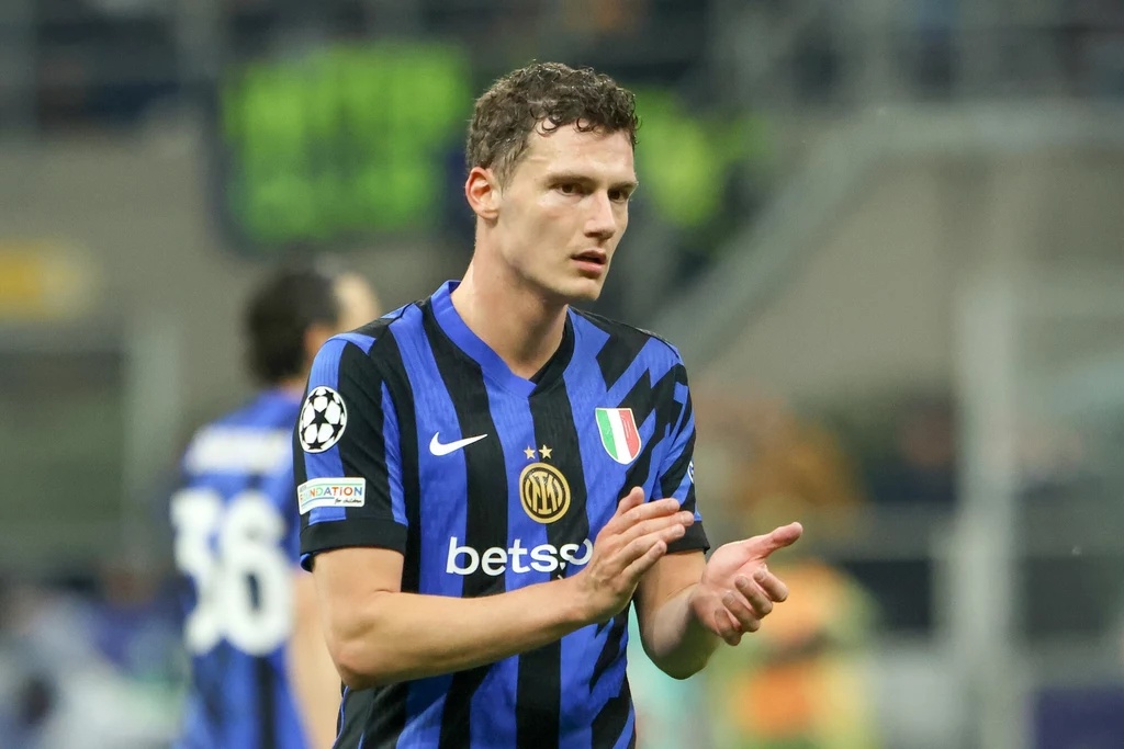 Benjamin Pavard Piłkarz w niebiesko-czarnej koszulce Interu Mediolan klaszcze w dłonie, wokół rozmyte sylwetki innych zawodników i fragment boiska.