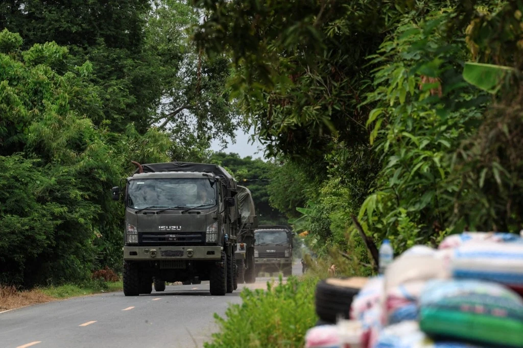 Kolejny dzień eskalacji na linii Tajlandia-Kambodża Kolumna wojskowych ciężarówek poruszająca się asfaltową drogą przez zielony, zalesiony teren, przy której widoczne są poukładane worki lub paczki