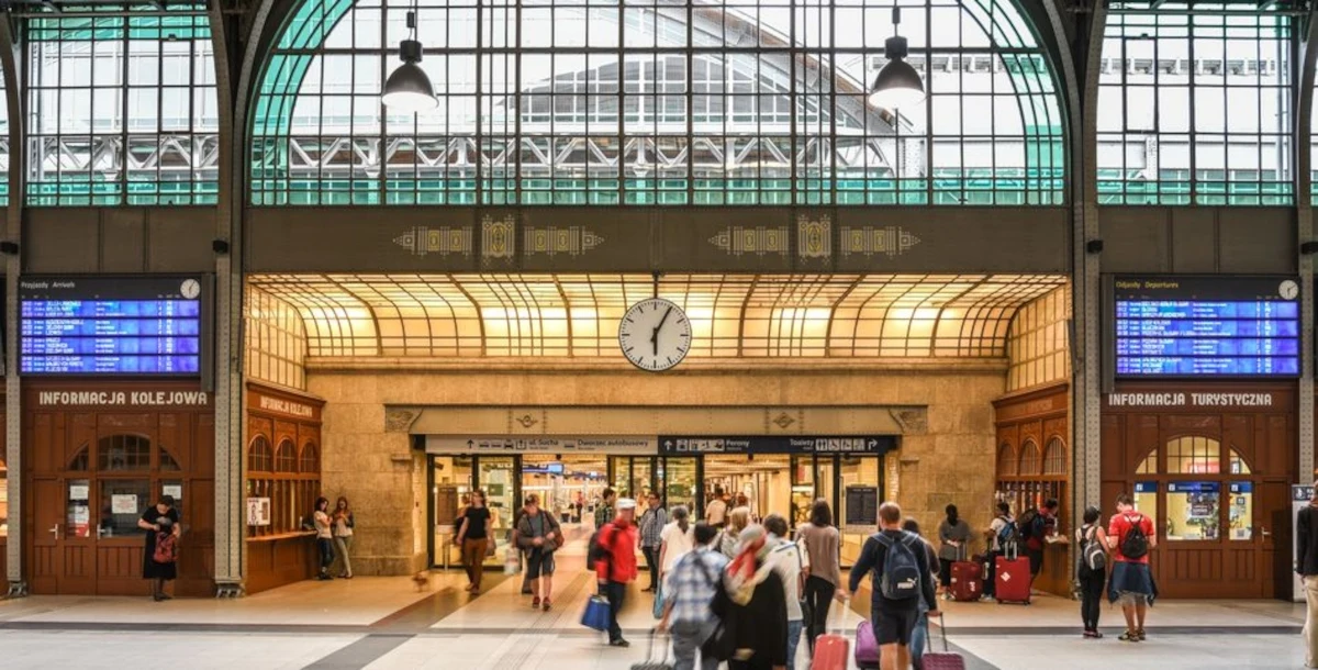 Wrocław Główny najpopularniejszym dworcem kolejowym w Polsce. Ruchliwa hala dworca kolejowego z dużym zegarem pośrodku, nad wejściem, licznymi pasażerami z bagażami oraz tablicami informacyjnymi po bokach.