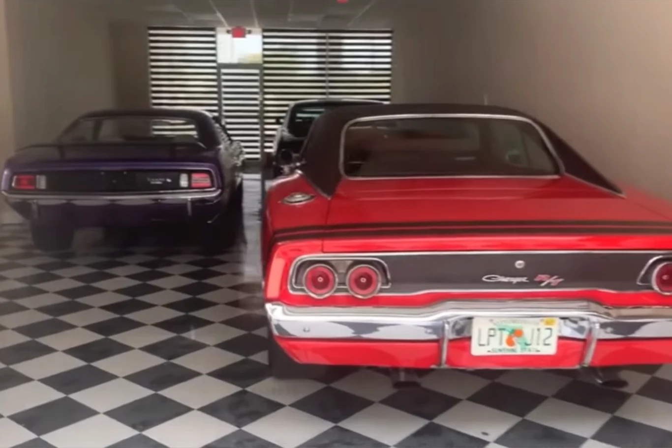 Dwa klasyczne amerykańskie samochody, czerwony Dodge Charger R/T oraz ciemnofioletowy samochód muscle car, zaparkowane na czarno-białej szachownicy podłogowej w zamkniętym pomieszczeniu z przeszklonym wejściem.