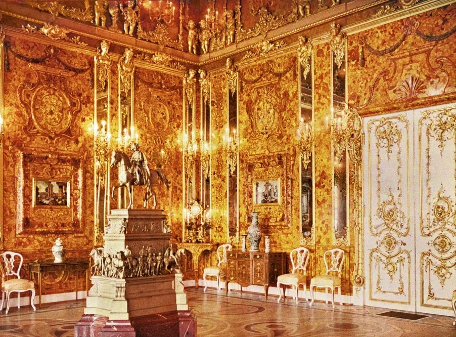 Wnętrze bogato zdobionego pomieszczenia z licznymi złotymi i bursztynowymi dekoracjami na ścianach, rzeźbionymi panelami, kryształowymi żyrandolami oraz eleganckimi białymi krzesłami; centralnie umieszczony okazały posąg konny na postumencie.