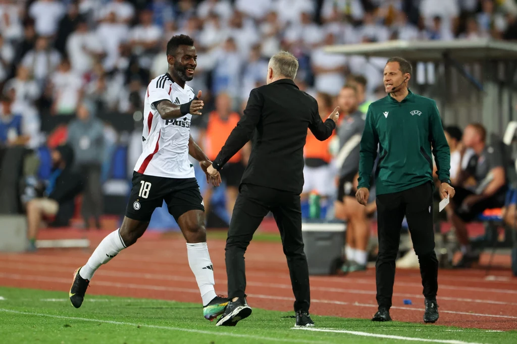 Legia uratowała remis w 88. minucie. Do siatki trafił wówczas Jean-Pierre Nsame Piłkarz w stroju Legii Warszawa biegnie w stronę trenera z rozłożonymi rękami, obaj są wyraźnie zadowoleni z sytuacji, w tle widoczny trener drużyny przeciwnej oraz ławka rezerwowych na stadionie pełnym kibiców.