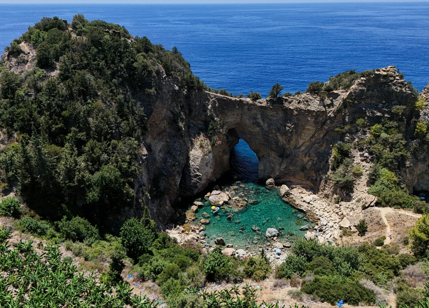 Turecka Antalya jest jedną z ulubionych turystycznych destynacji rosyjskich turystów Malowniczy skalisty łuk nad niewielką zatoką z turkusową wodą, otoczony bujną zielenią i stromymi klifami, przy bezchmurnym, błękitnym niebie.