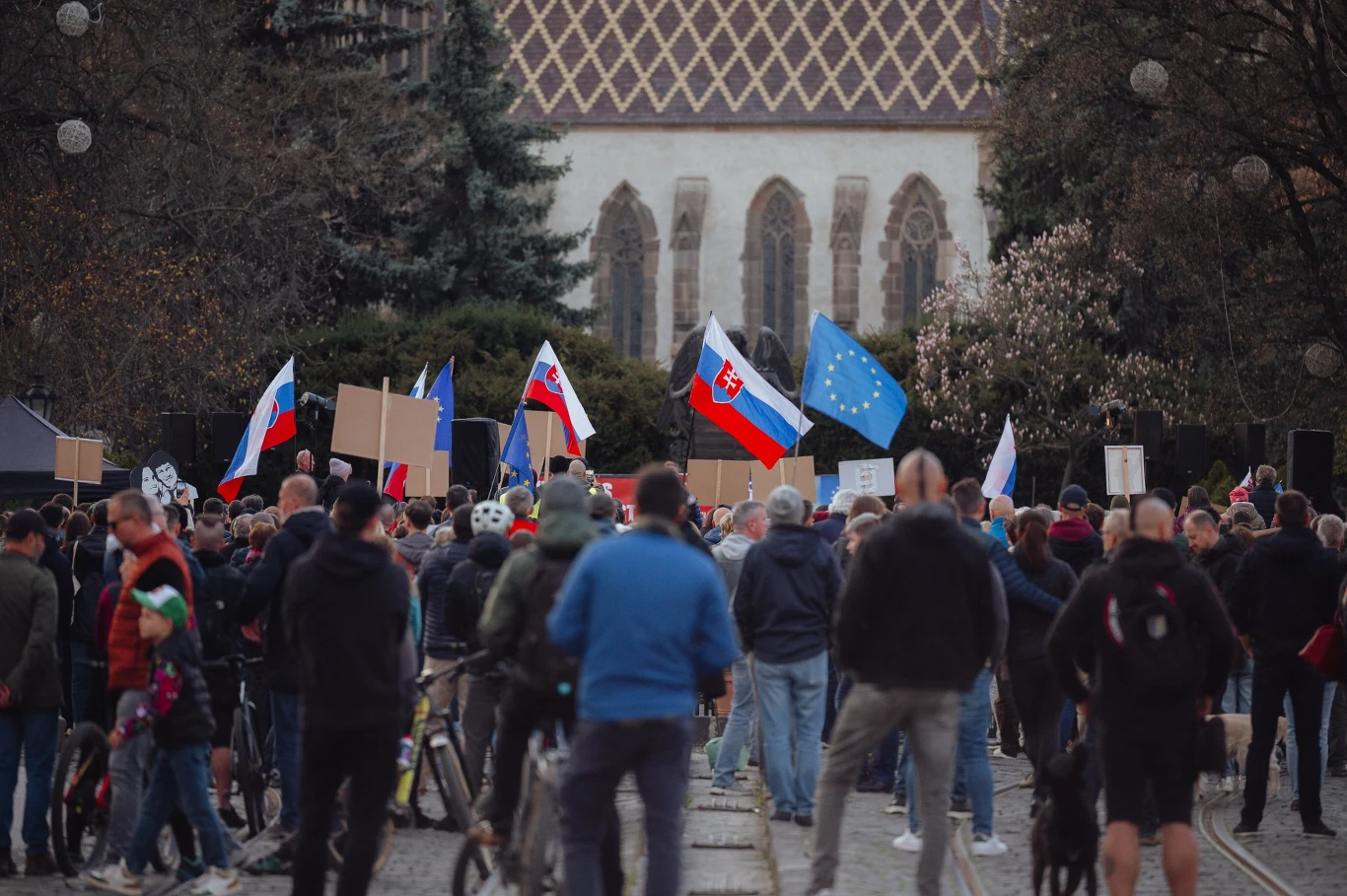 Część Słowaków chce akcesji do Rosji. Jest nowy sondaż. Zdj. ilustracyjne Tłum ludzi zgromadzonych na ulicy w centrum miasta, trzymających flagi Słowacji, Rosji oraz Unii Europejskiej, a także transparenty bez widocznych napisów, w tle zabytkowy budynek kościoła