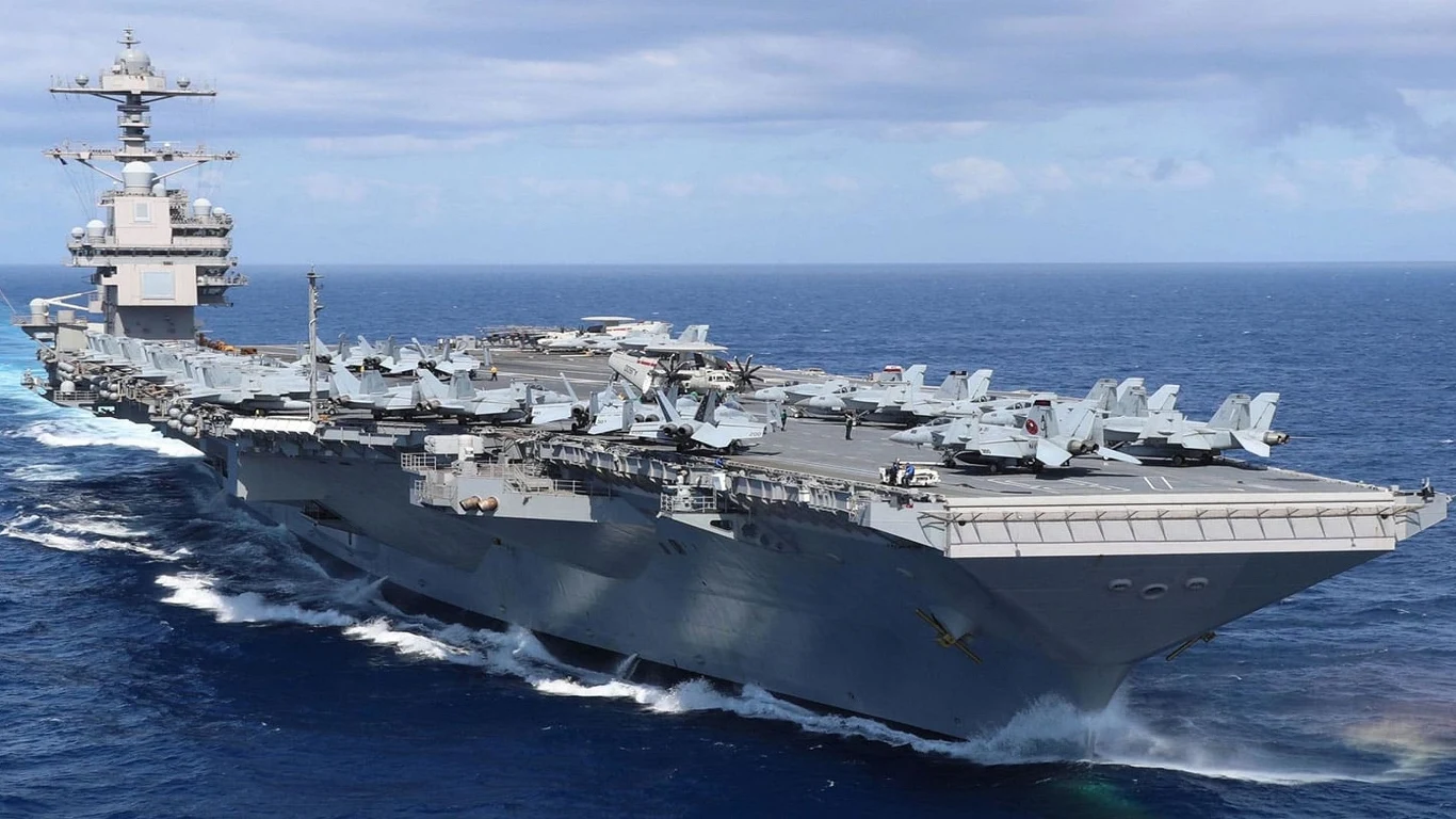 Największy lotniskowiec świata, USS Gerald R. Ford, przybył do Europy Nowoczesny lotniskowiec płynący po oceanie, na pokładzie umieszczone samoloty myśliwskie i inne maszyny wojskowe, wyraźne fale na wodzie oraz słoneczna pogoda z lekkim zachmurzeniem.