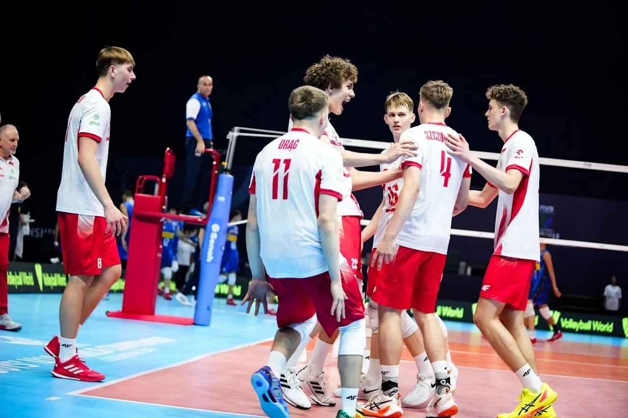 Grupa młodych siatkarzy w biało-czerwonych strojach świętuje zdobyty punkt na boisku podczas meczu siatkówki, z widocznymi emocjami i energią wśród zawodników.