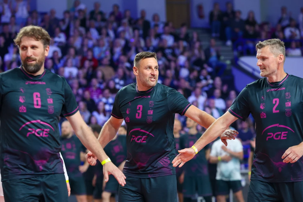 Od lewej: Dawid Murek, Marcin Wika i Krzysztof Gierczyński na pożegnalnym meczu Andrzeja Wrony Trzech siatkarzy w czarnych strojach zespołu PGE witających się na boisku podczas meczu, w tle widownia pełna kibiców.