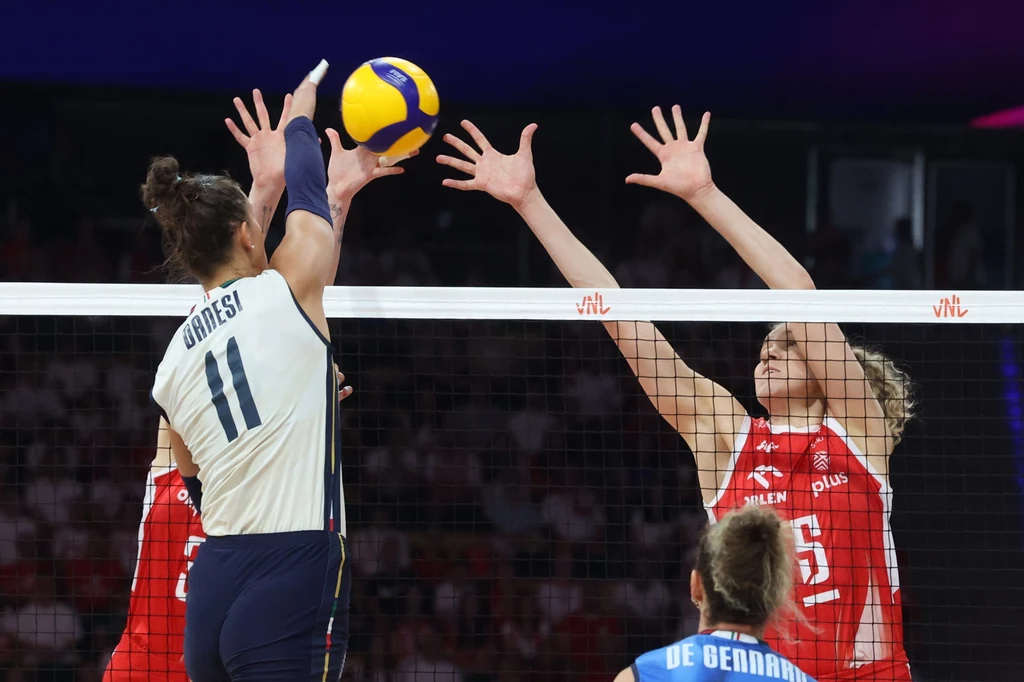 Liga Narodów siatkarek. Polska miała duży problem z Włochami Zawodniczki drużyny siatkarskiej podczas dynamicznej walki przy siatce, jedna z nich próbuje przebić piłkę, a przeciwniczki w czerwonych strojach wykonują blok.
