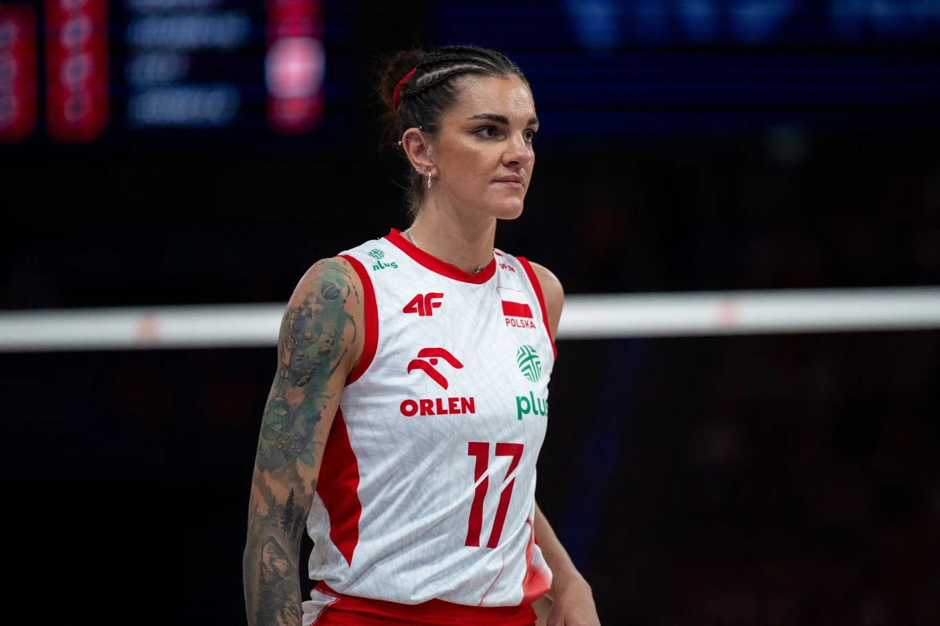Malwina Smarzek Siatkarka w stroju reprezentacji Polski z widocznymi tatuażami na rękach stoi na boisku podczas meczu, skupiona na grze.