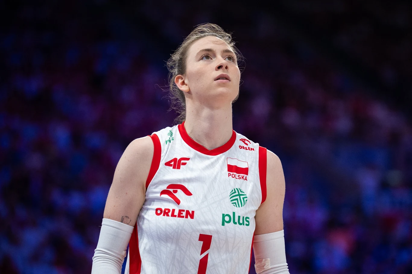 Zawodniczka w stroju reprezentacji Polski do siatkówki, skupiona na tle rozmytego stadionu, wyraźnie przygotowująca się do kolejnej akcji w grze.