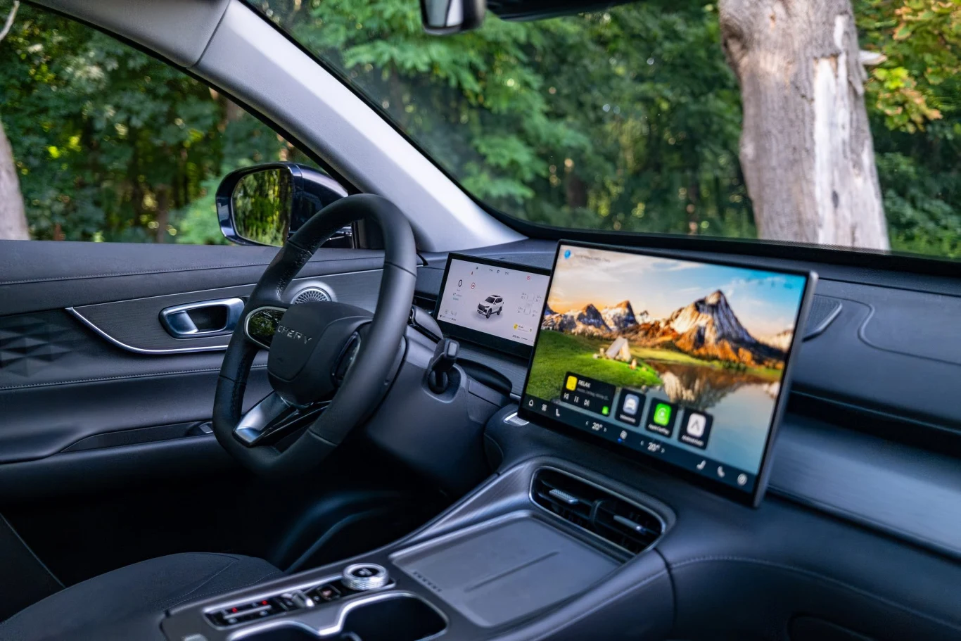 W przemyślanie urządzonym wnętrzu dominuje ekran systemu multimedialnego Nowoczesne, eleganckie wnętrze samochodu z dwoma dużymi ekranami na desce rozdzielczej, cyfrowym kokpitem oraz systemem multimedialnym, widoczne elementy wykończenia z wysokiej jakości materiałów, widok na zalesione otoczenie za szybą.