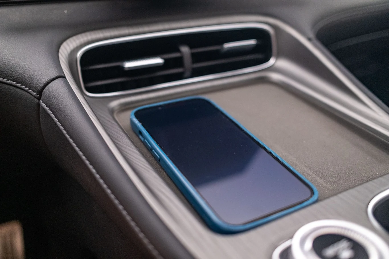 Ładowarka o mocy 50 W została wyposażona w układ chłodzenia. Działa bez zarzutu Nowoczesny smartfon w niebieskim etui leżący na konsoli środkowej samochodu obok kratek nawiewu i elementów sterujących kokpitu.