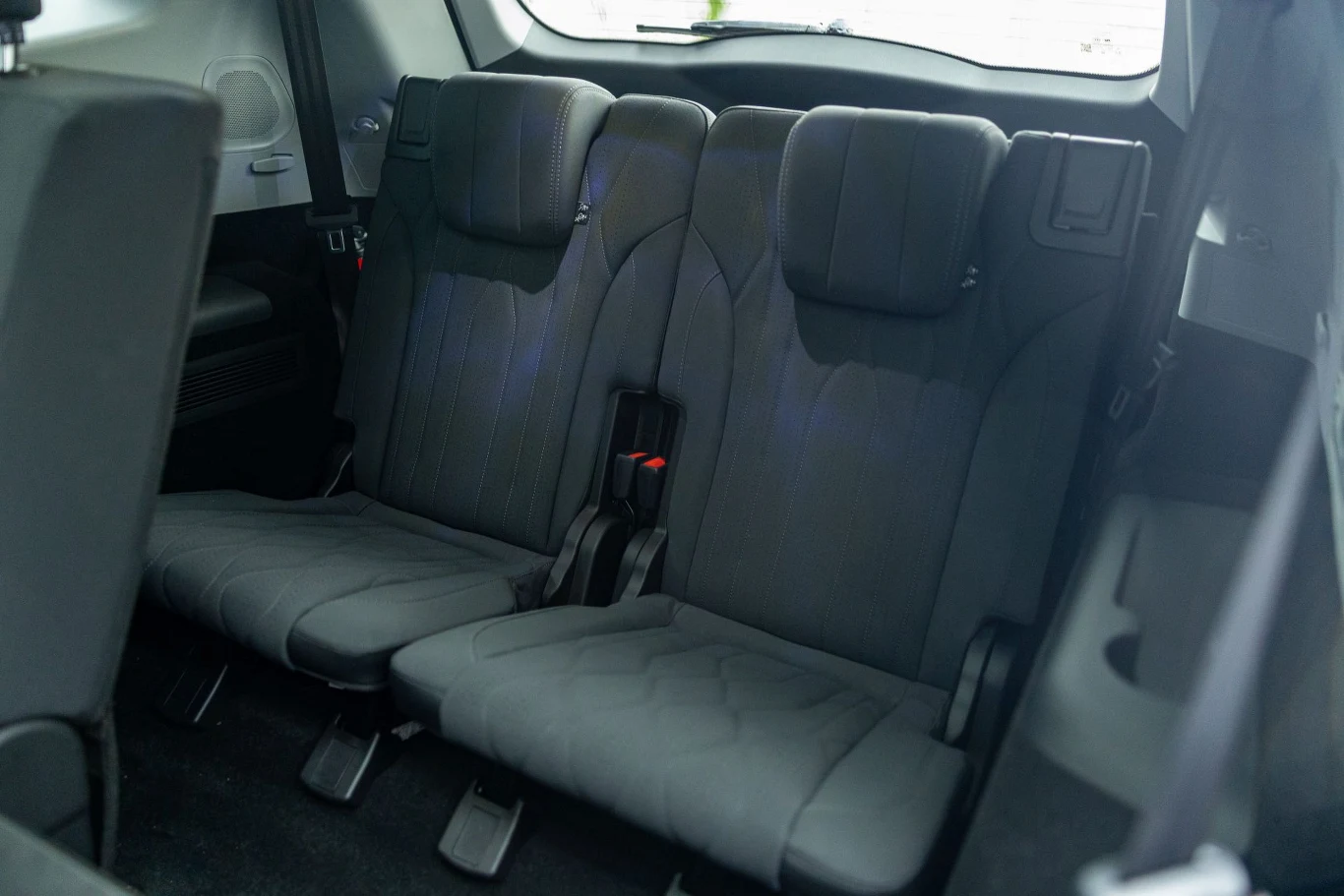 Dodatkowe miejsca w trzecim rzędzie idealnie sprawdzą się na krótkie wycieczki Trzeci rząd siedzeń w samochodzie osobowym, tapicerka w kolorze ciemnoszarym, składane oparcia oraz zagłówki, czyste wnętrze pojazdu.