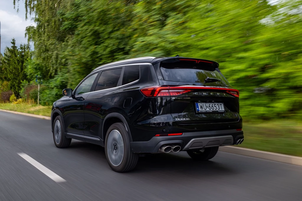 Czarny SUV jedzie po asfaltowej drodze otoczonej zielenią, tył samochodu widoczny z tablicą rejestracyjną i charakterystycznymi reflektorami LED.
