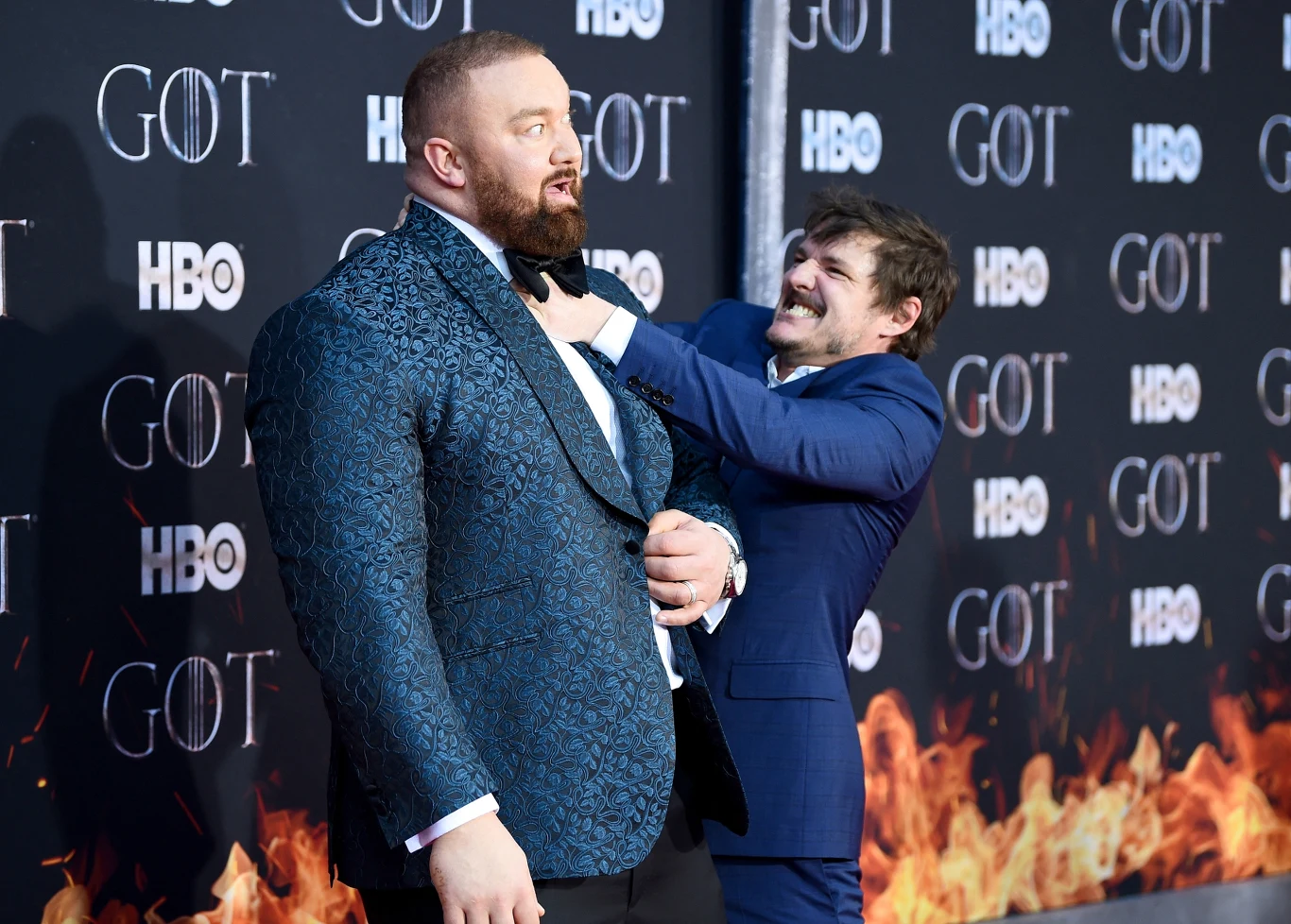 Hafthor Julius Bjornsson i Pedro Pascal promujący serial "Gra o tron" Dwóch mężczyzn w eleganckich garniturach pozuje na tle ścianki z logo HBO i GOT, jeden z nich chwyta drugiego za krawat w żartobliwy sposób, wokół panuje atmosfera wydarzenia medialnego.
