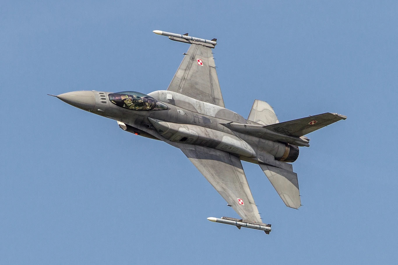 Wojna w Ukrainie. Polska poderwała myśliwce w związku z nocnymi atakami Rosji (Zdj. ilustracyjne) Myśliwiec wojskowy F-16 w barwach polskich sił powietrznych lecący na tle nieba, uzbrojony w pociski, widoczna kabina z pilotem.