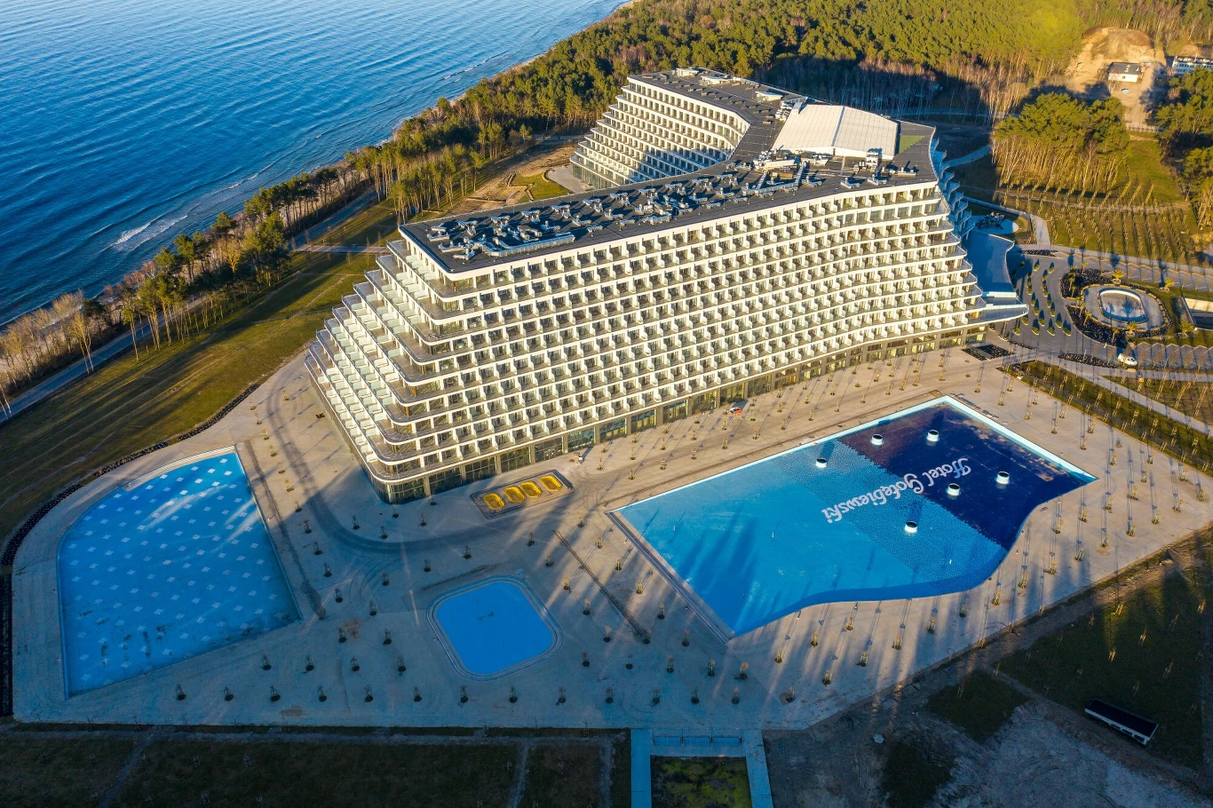 Chorwackie media piszą o hotelu Gołębiewskim. Inwestycja zagrozi niemieckim kurortom? Współczesny hotel o charakterystycznej, tarasowej architekturze z dużymi przeszklonymi balkonami, położony nad samym morzem w otoczeniu lasu. Przed budynkiem znajdują się dwa baseny o regularnych kształtach, widoczna jest również pusta przestrzeń i ter...