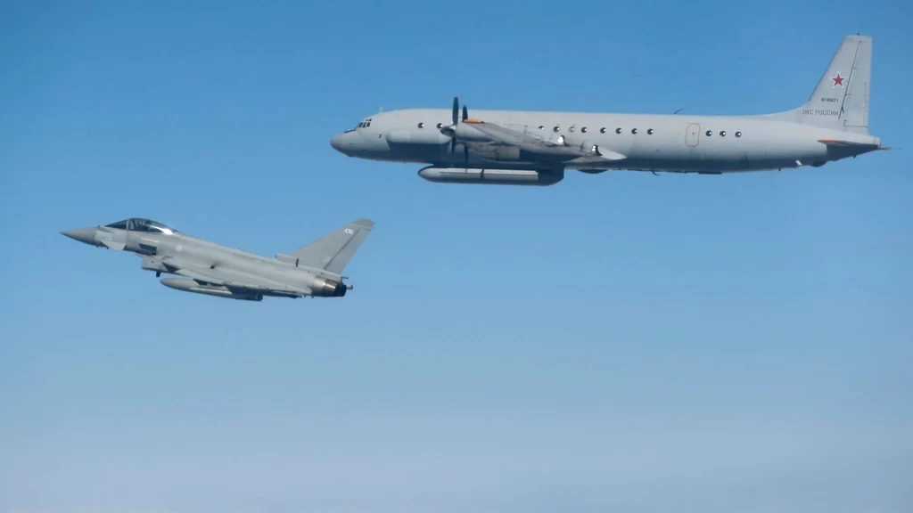 Brytyjski Eurofighter Typhoon podczas przechwycenia rosyjskiego Ił-20 nad Bałtykiem Dwa wojskowe samoloty lecące równolegle na tle błękitnego nieba, jeden z nich to większy samolot z czerwoną gwiazdą na ogonie, drugi to myśliwiec o charakterystycznych smukłych kształtach.