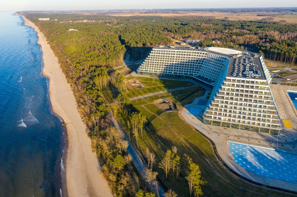 Nowoczesny budynek hotelowy o charakterystycznej, kaskadowej architekturze położony nad morzem, otoczony lasem i piaszczystą plażą, z przestronnymi terenami zielonymi oraz basenem.