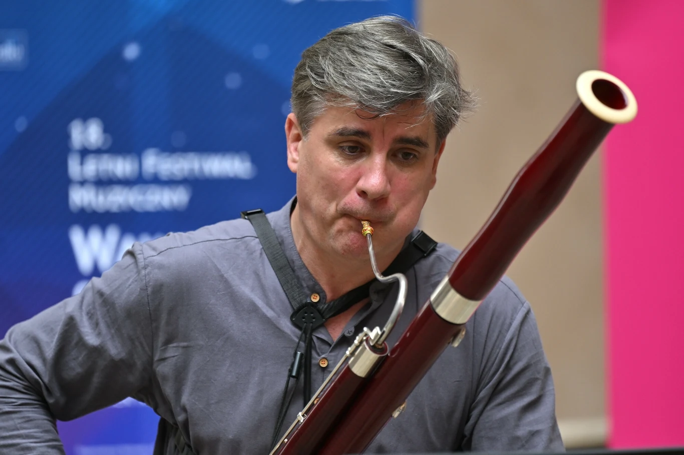 Na Wawel o zmierzchu pojawi się m.in LLLeggiero Woodwind Trio. Na zdjęciu: Damian Lipień Mężczyzna grający na fagocie w trakcie koncertu, tło stanowią kolorowe plakaty i rozmyte napisy festiwalu muzycznego.