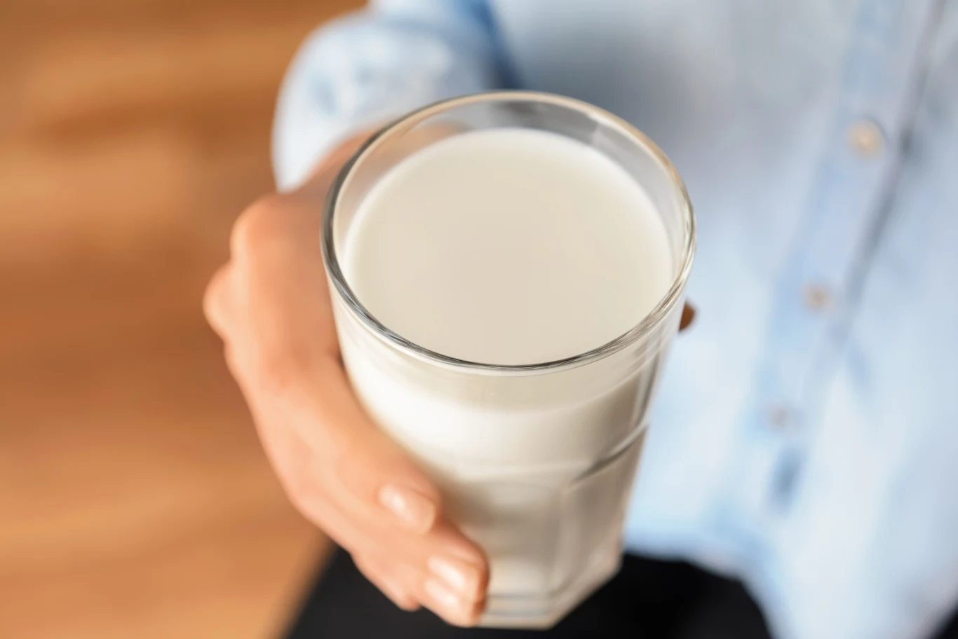 Kefir wraca do łask jako naturalne wsparcie dla jelit. Sprawdź, ile naprawdę warto go pić, żeby sobie pomóc, a nie zaszkodzić Szklanka kefiru trzymana w dłoni, widoczne szkło i kremowy napój na tle rozmytej niebieskiej koszuli.
