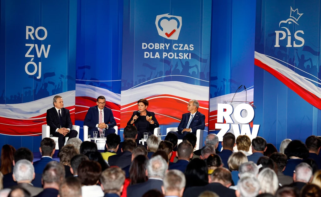 Piotr Gliński, Mateusz Morawiecki, Beata Szydło, Jerzy Kwieciński podczas panelu na kongresie programowym PiS w Katowicach w 2019 roku. Dziś też PiS chce postawić na ofensywę programową Debata polityczna z udziałem czterech osób siedzących na scenie, w tle widoczne banery z hasłami Rozwój, Dobry czas dla Polski oraz logo partii politycznej, przed sceną liczna publiczność.