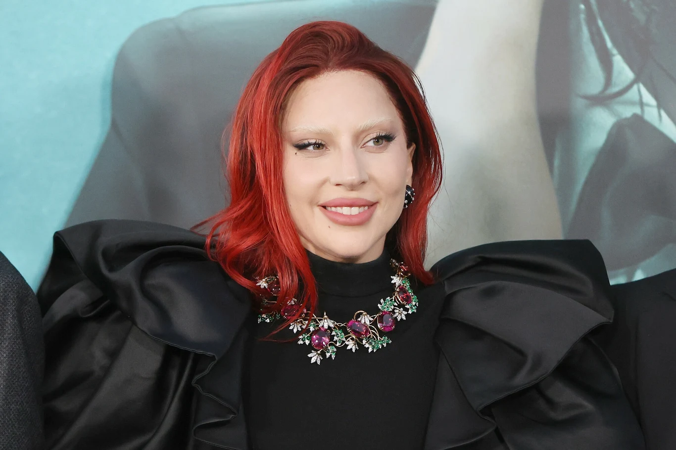 Lady Gaga będzie kontynuowała współpracę z Timem Burtonem Kobieta o rudych włosach uśmiecha się, ubrana w czarną suknię z szerokimi ramionami i wyrazistą, błyszczącą kolia z kolorowymi kamieniami. Tło utrzymane jest w jasnych odcieniach niebieskiego.
