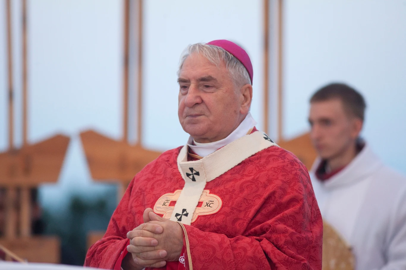 Abp Józef Kowalczyk trafił do szpitala Starszy duchowny w czerwonej szacie liturgicznej, stoi ze złożonymi dłońmi, w tle znajduje się drugi mężczyzna również ubrany w szatę liturgiczną.