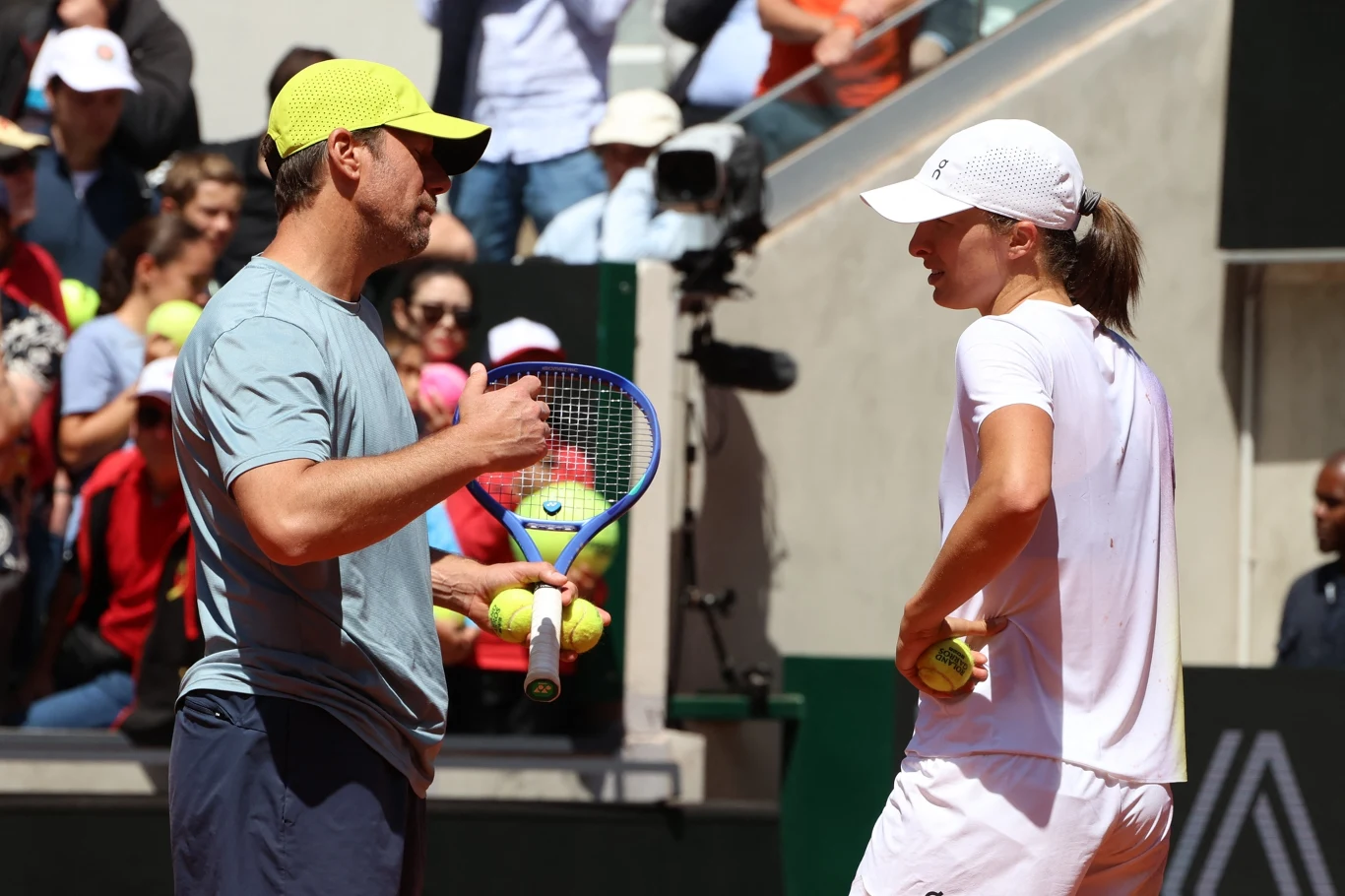 Wim Fissette i Iga Świątek Trener rozmawia z tenisistką na korcie podczas przerwy w trakcie meczu, w tle widoczna jest publiczność oraz operator z kamerą, a obie osoby są ubrane w sportowe stroje