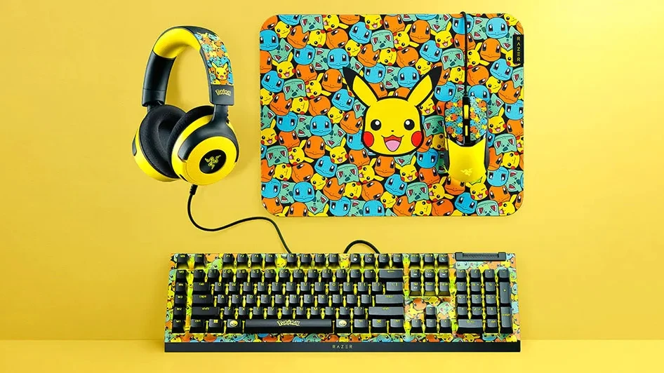 Zestaw komputerowych akcesoriów z motywem Pikachu, w skład którego wchodzą klawiatura, myszka, podkładka pod mysz i słuchawki, wszystkie w energetycznych barwach żółci i czerni oraz pokryte grafikami Pikachu i innych Pokémonów
