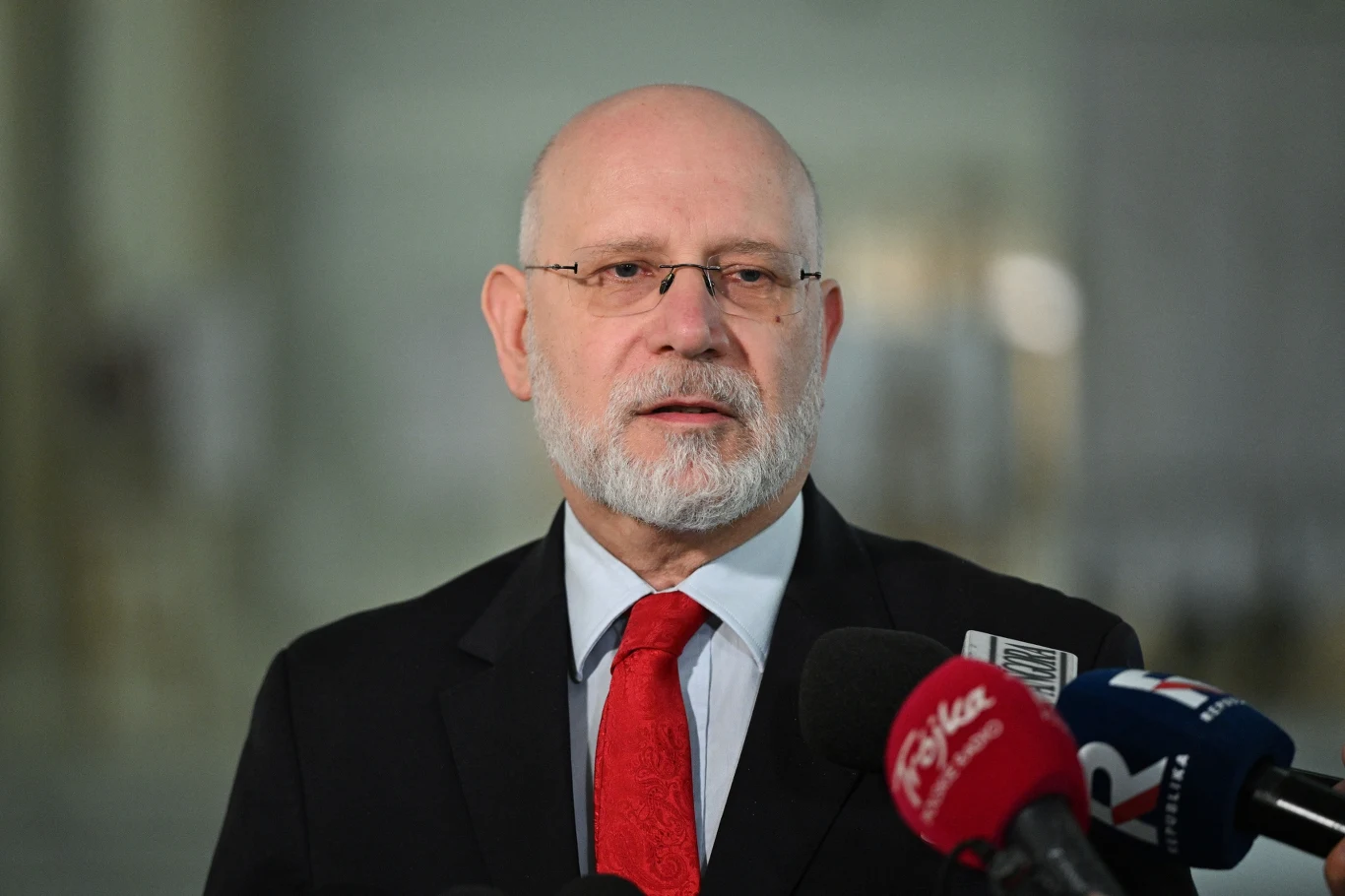 Maciej Świrski odwołany ze stanowiska szefa KRRiT. Wydał oświadczenie Mężczyzna w okularach i z siwą brodą w garniturze z czerwoną krawatą przemawia do mikrofonów różnych stacji telewizyjnych.