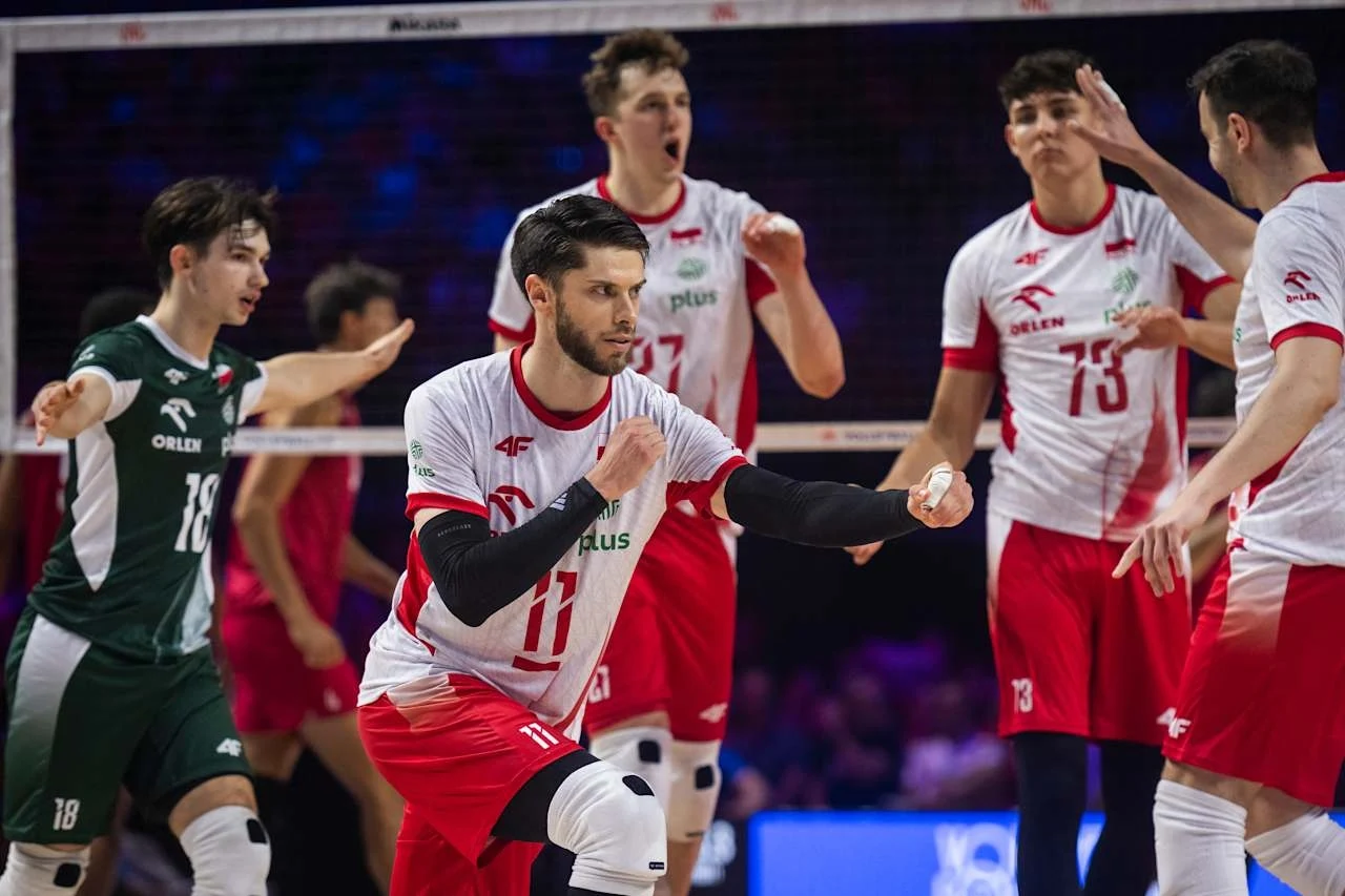 Grupa polskich siatkarzy ubranych w narodowe stroje podczas meczu, jeden z zawodników w dynamicznej pozie wykonuje zagranie, pozostali gracze w tle przygotowują się do kolejnego ruchu, atmosfera sportowej rywalizacji.