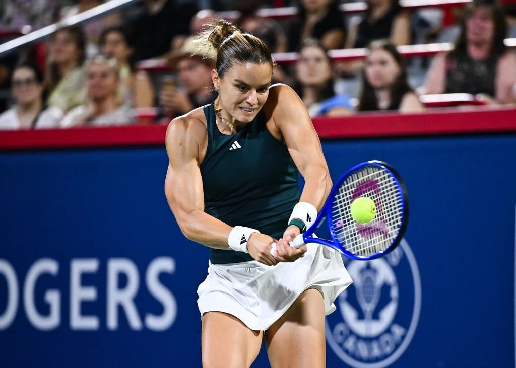 Maria Sakkari Tenisistka uderzająca piłkę rakietą podczas meczu, na drugim planie widać zapełnione trybuny i napis reklamowy.