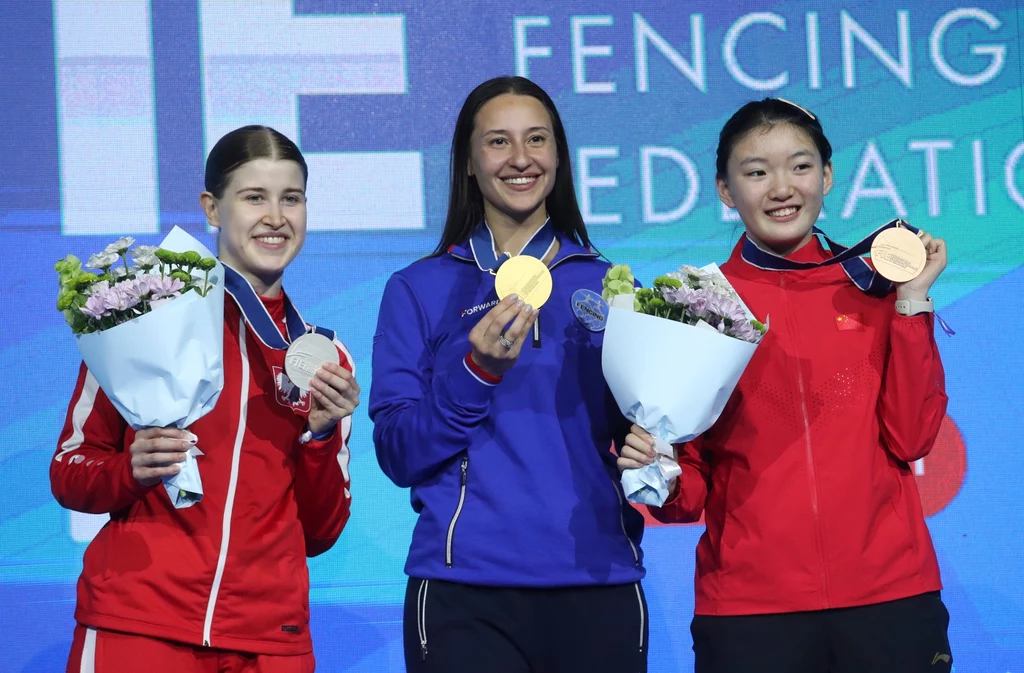 Na podium MŚ w szermierce zawsze staję cztery zawodniczki. Tym razem zabrakło Ukrainki Aliny Komaszczuk. Od lewej: Zuzanna Cieślar, Jana Jegorian i Qimiao Pan Trzy medalistki stoją na podium, uśmiechają się i trzymają swoje medale oraz bukiety kwiatów, tło z logotypem federacji szermierczej.