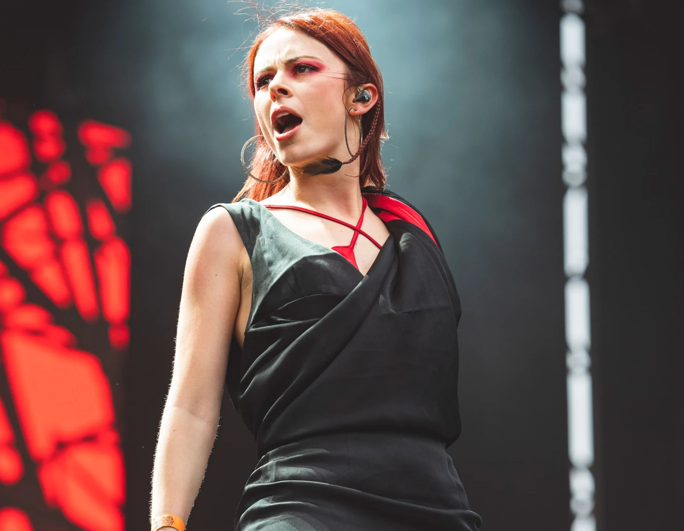 Jennifer Haben (Beyond The Black) w akcji Kobieta występująca na scenie w czarnym stroju z czerwonymi akcentami, z mikrofonem przy twarzy, w dynamicznej pozie, tło rozmazane z czerwonymi i czarnymi elementami oświetlenia scenicznego.
