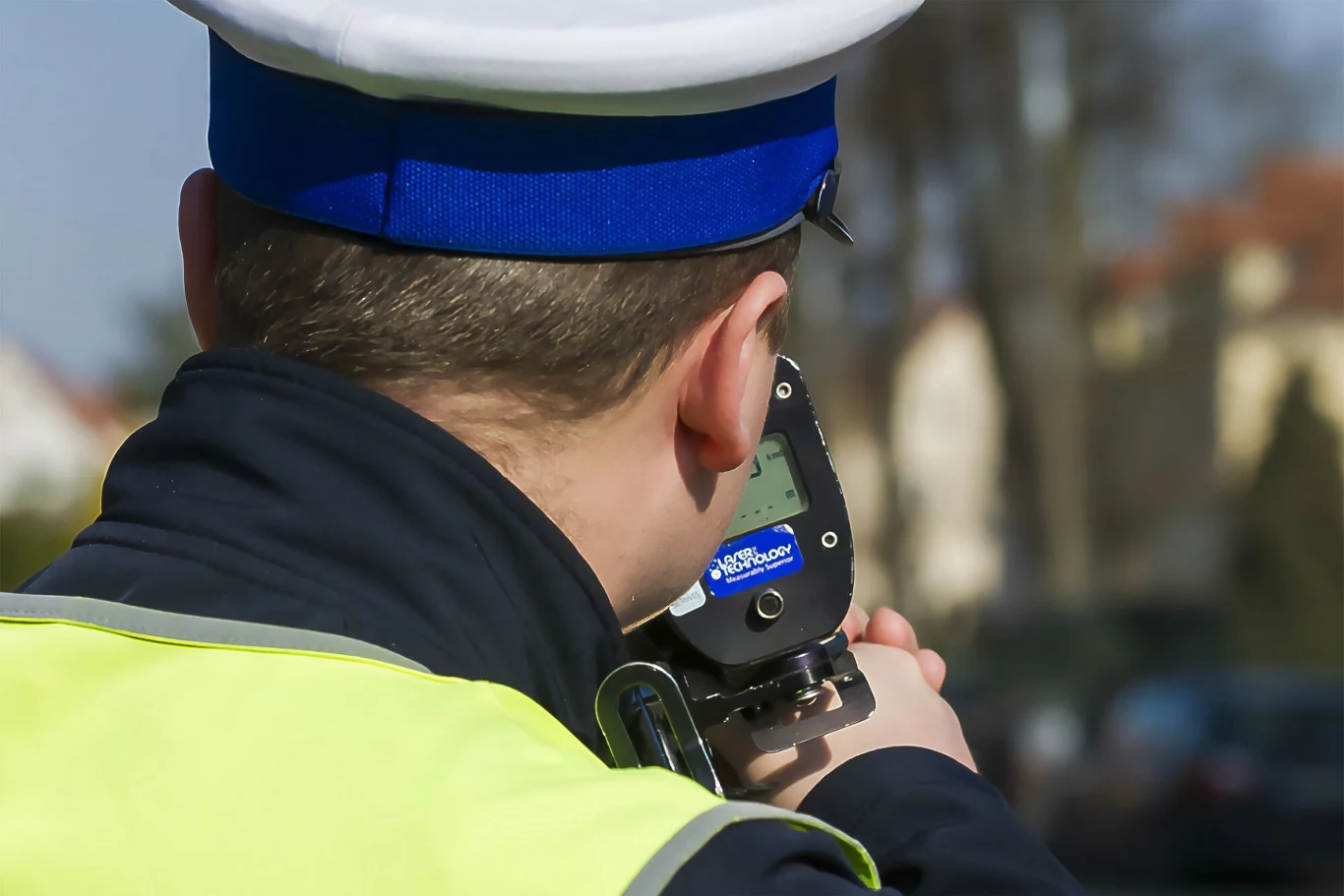 Przekroczyłeś prędkość w Estonii? Policja pozwoli ci wybrać. Policjant w mundurze oraz czapce mierzy prędkość urządzeniem radarowym, skupiając się na drodze przed sobą.