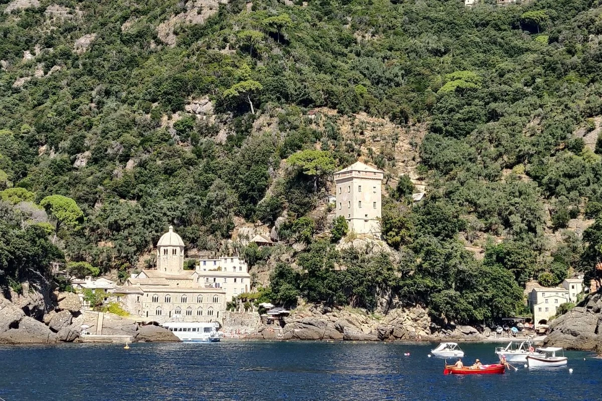 Kamienny klasztor i inne historyczne budynki położone są u podnóża zalesionego wzgórza nad lazurową wodą, w pobliżu brzegu cumują niewielkie łodzie.