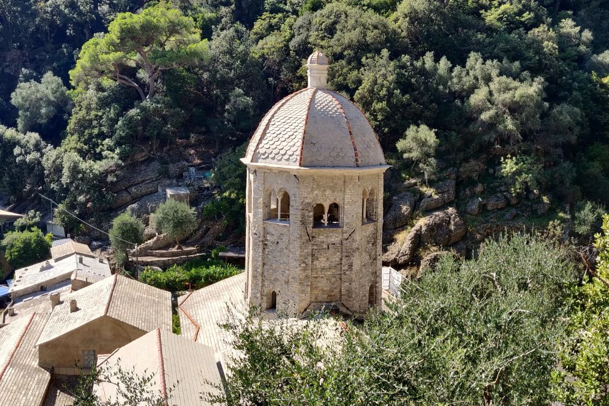 Kamienna wieża z kopułą otoczona dachami budynków, położona wśród bujnej zieleni i drzew na zboczu wzgórza.
