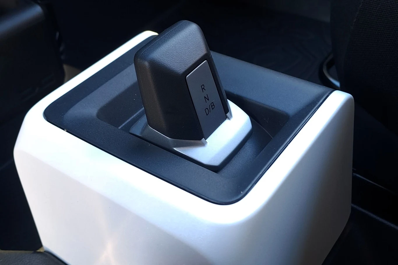 Dźwignia zmiany biegów w nowoczesnym samochodzie, umieszczona na konsoli środkowej, w otoczeniu czarno-białych elementów wnętrza pojazdu.