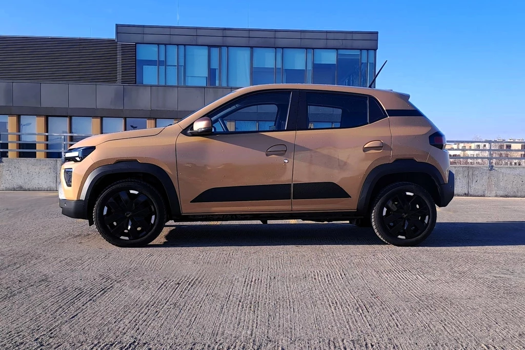 Brązowy kompaktowy SUV stoi na parkingu z betonową nawierzchnią na tle nowoczesnego, przeszklonego budynku.
