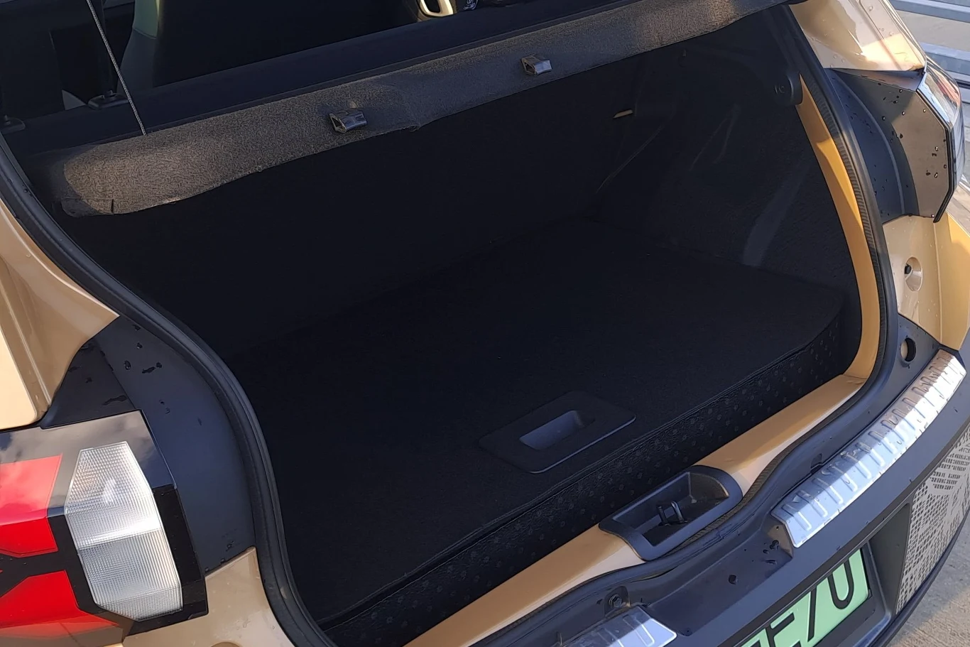 Otwarta przestronna bagażnik samochodu osobowego w jasnożółtym kolorze, z dobrze widocznymi elementami wnętrza oraz fragmentem tylnej lampy i zderzaka.