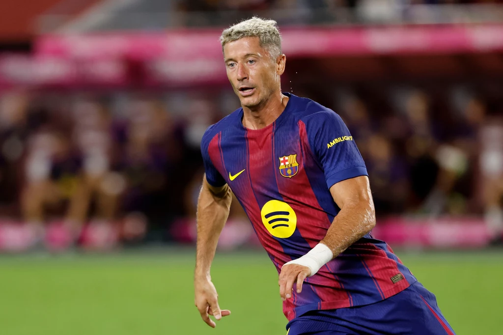 Robert Lewandowski Piłkarz w stroju FC Barcelony biegnie po murawie podczas meczu, skoncentrowany na grze, w tle rozmazany stadion i kibice.